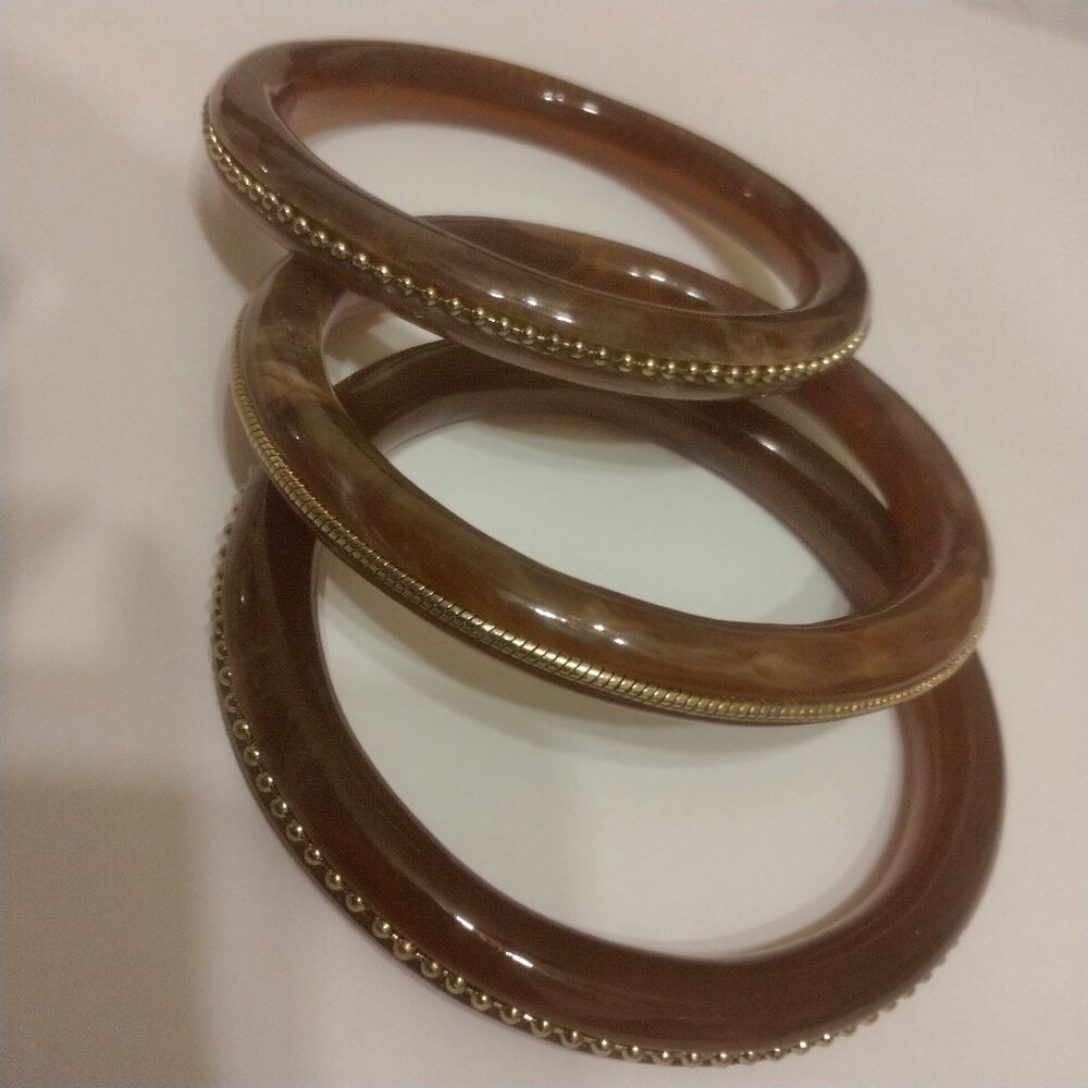 WOMENS LARGE SIZE HARD PLASTIC BANGLE BRACELETS WITH DECORATIVE GOLDTONE TRIM.